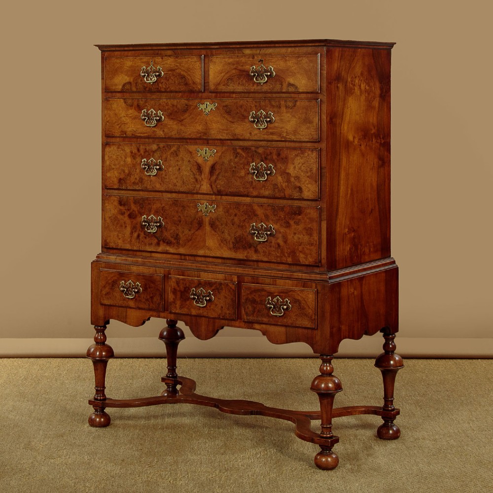 A 1930s Queen Anne Revival burr walnut chest on stand featuring multiple graduated drawers, decorative brass handles, turned legs, and a shaped apron. View III