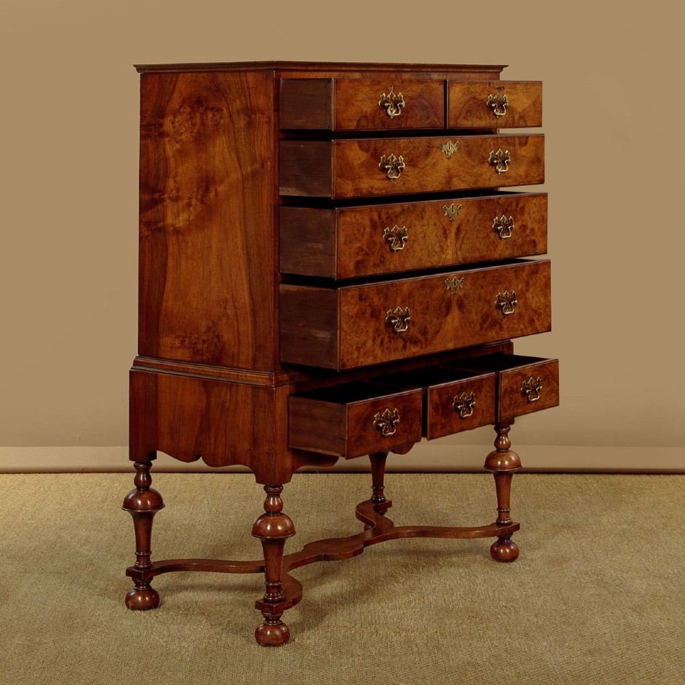 A 1930s Queen Anne Revival burr walnut chest on stand featuring multiple graduated drawers, decorative brass handles, turned legs, and a shaped apron. View IV