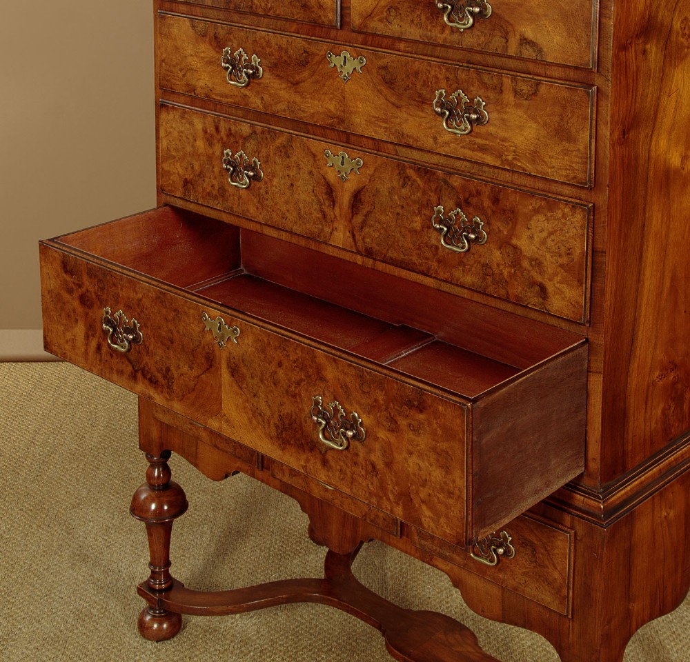A 1930s Queen Anne Revival burr walnut chest on stand featuring multiple graduated drawers, decorative brass handles, turned legs, and a shaped apron. View VI