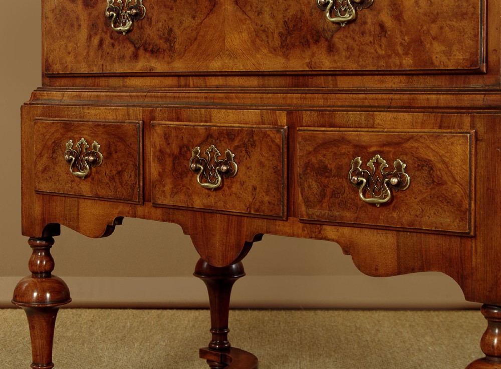 A 1930s Queen Anne Revival burr walnut chest on stand featuring multiple graduated drawers, decorative brass handles, turned legs, and a shaped apron. View VIII
