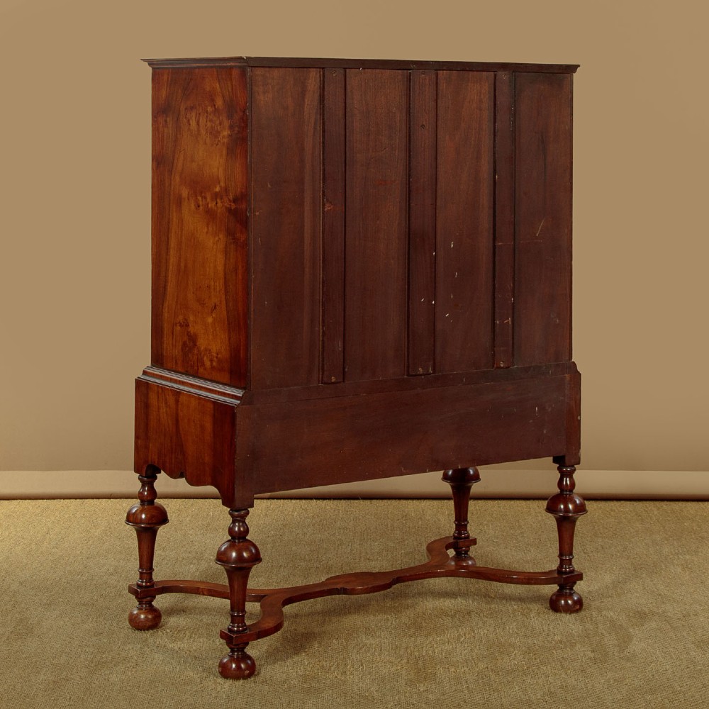 A 1930s Queen Anne Revival burr walnut chest on stand featuring multiple graduated drawers, decorative brass handles, turned legs, and a shaped apron. View XI
