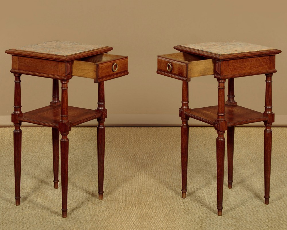 A pair of slender Edwardian oak lamp tables featuring inset marble tops, single drawers with brass ring pulls, turned tapered legs, and lower tier shelves. View III