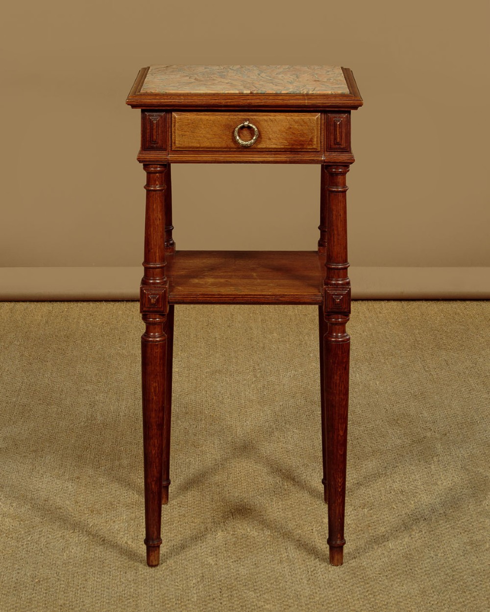 A pair of slender Edwardian oak lamp tables featuring inset marble tops, single drawers with brass ring pulls, turned tapered legs, and lower tier shelves. View V