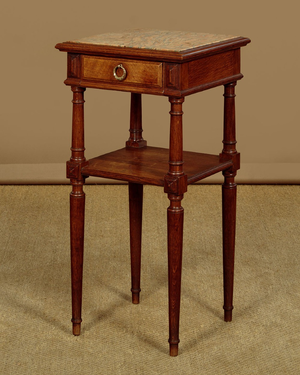 A pair of slender Edwardian oak lamp tables featuring inset marble tops, single drawers with brass ring pulls, turned tapered legs, and lower tier shelves. View VI