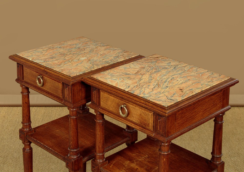 A pair of slender Edwardian oak lamp tables featuring inset marble tops, single drawers with brass ring pulls, turned tapered legs, and lower tier shelves. View VII