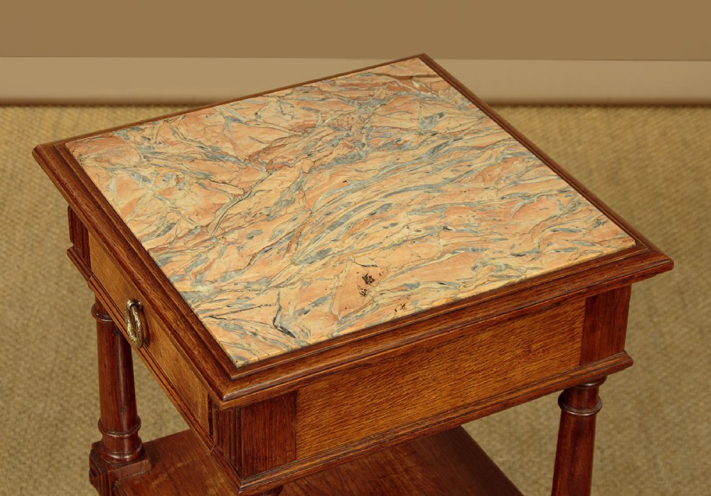 A pair of slender Edwardian oak lamp tables featuring inset marble tops, single drawers with brass ring pulls, turned tapered legs, and lower tier shelves. View VIII