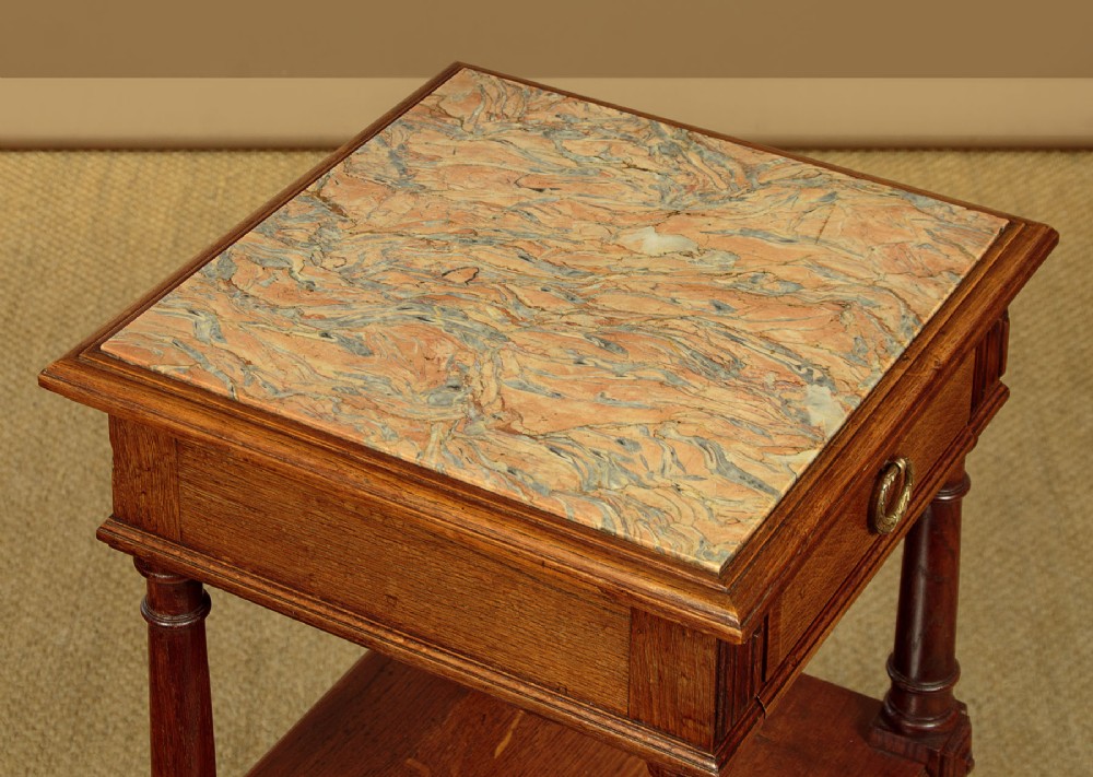 A pair of slender Edwardian oak lamp tables featuring inset marble tops, single drawers with brass ring pulls, turned tapered legs, and lower tier shelves. View IX