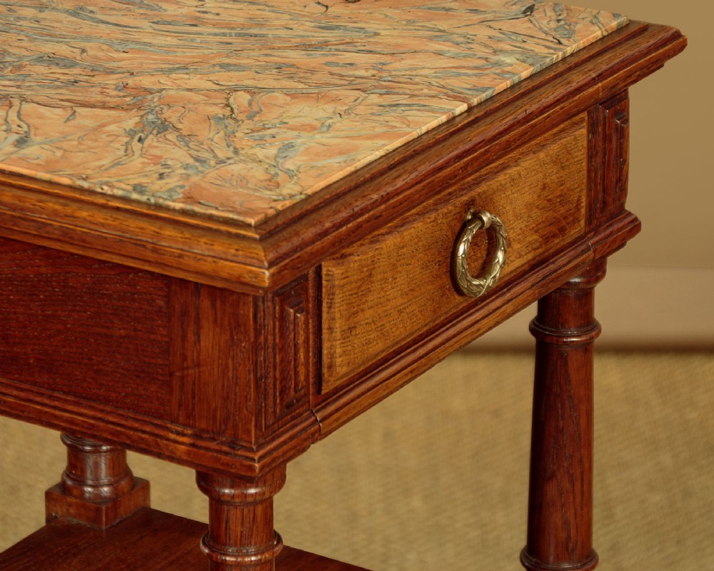 A pair of slender Edwardian oak lamp tables featuring inset marble tops, single drawers with brass ring pulls, turned tapered legs, and lower tier shelves. View X