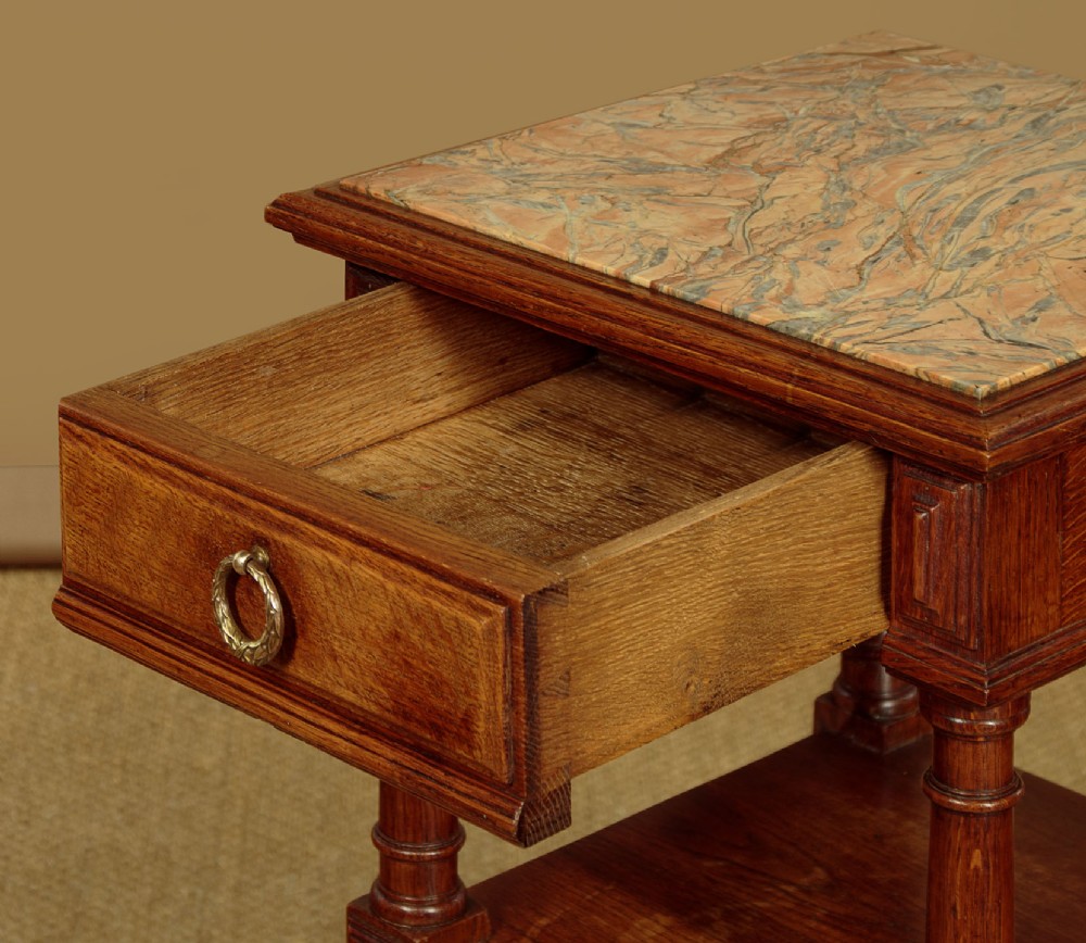 A pair of slender Edwardian oak lamp tables featuring inset marble tops, single drawers with brass ring pulls, turned tapered legs, and lower tier shelves. View XI