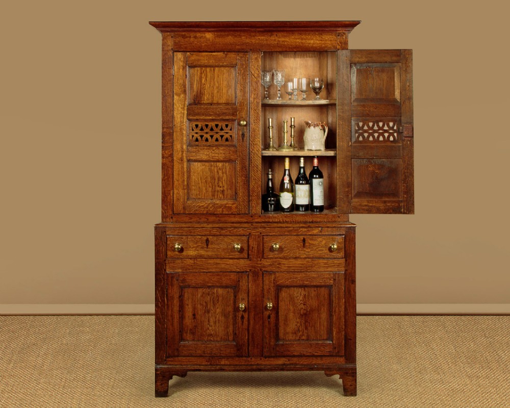 A two-part antique warm brown oak bread and cheese cupboard featuring upper doors with lattice ventilation fretwork over lower drawers and panelled cupboard doors. View II