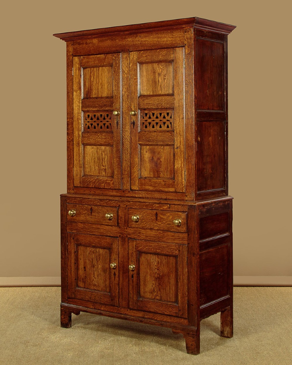 A two-part antique warm brown oak bread and cheese cupboard featuring upper doors with lattice ventilation fretwork over lower drawers and panelled cupboard doors. View III