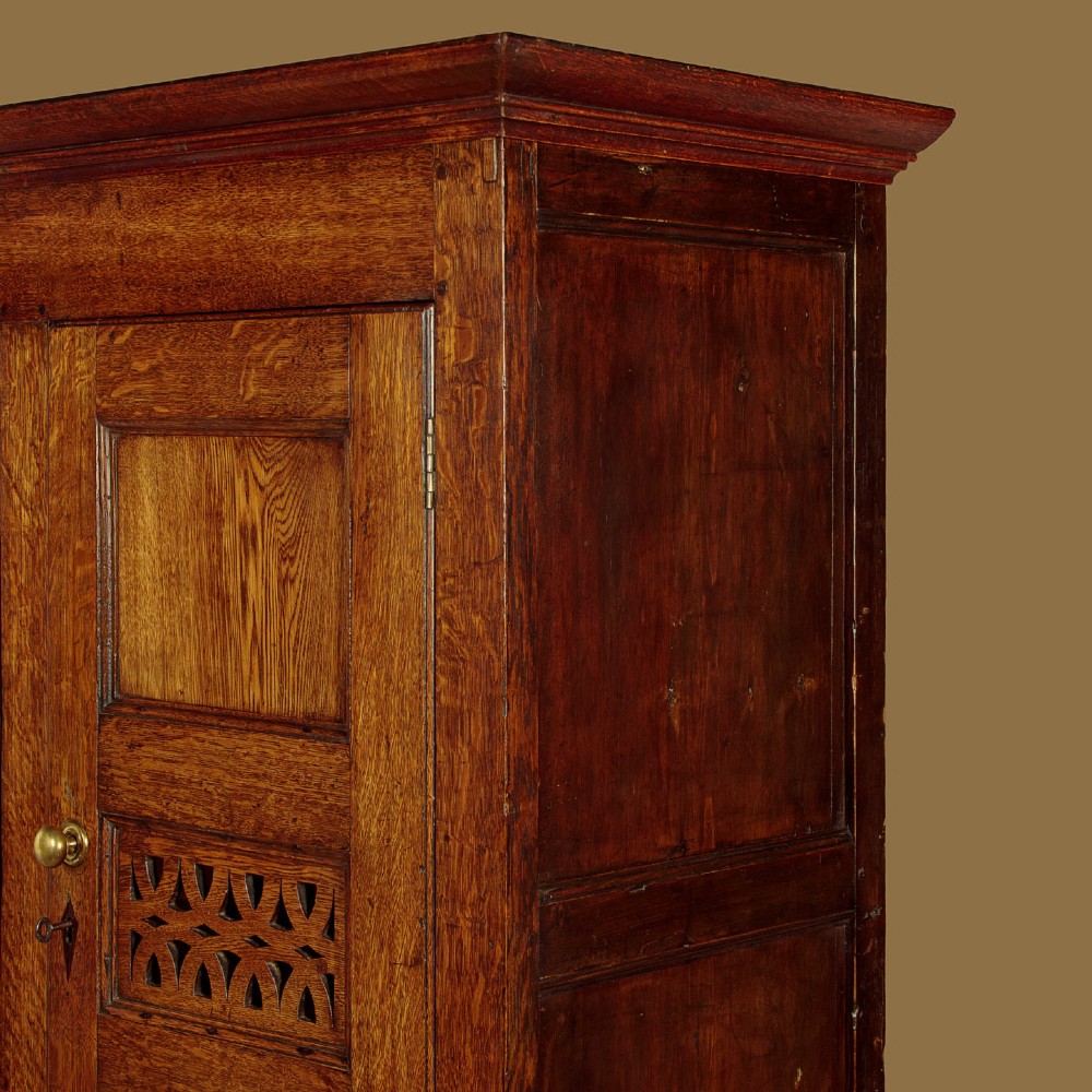 A two-part antique warm brown oak bread and cheese cupboard featuring upper doors with lattice ventilation fretwork over lower drawers and panelled cupboard doors. View V