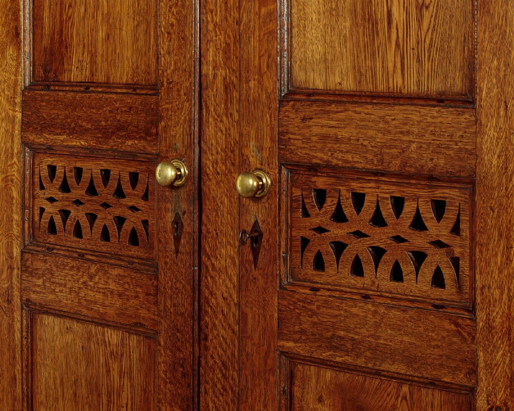 A two-part antique warm brown oak bread and cheese cupboard featuring upper doors with lattice ventilation fretwork over lower drawers and panelled cupboard doors. View VI