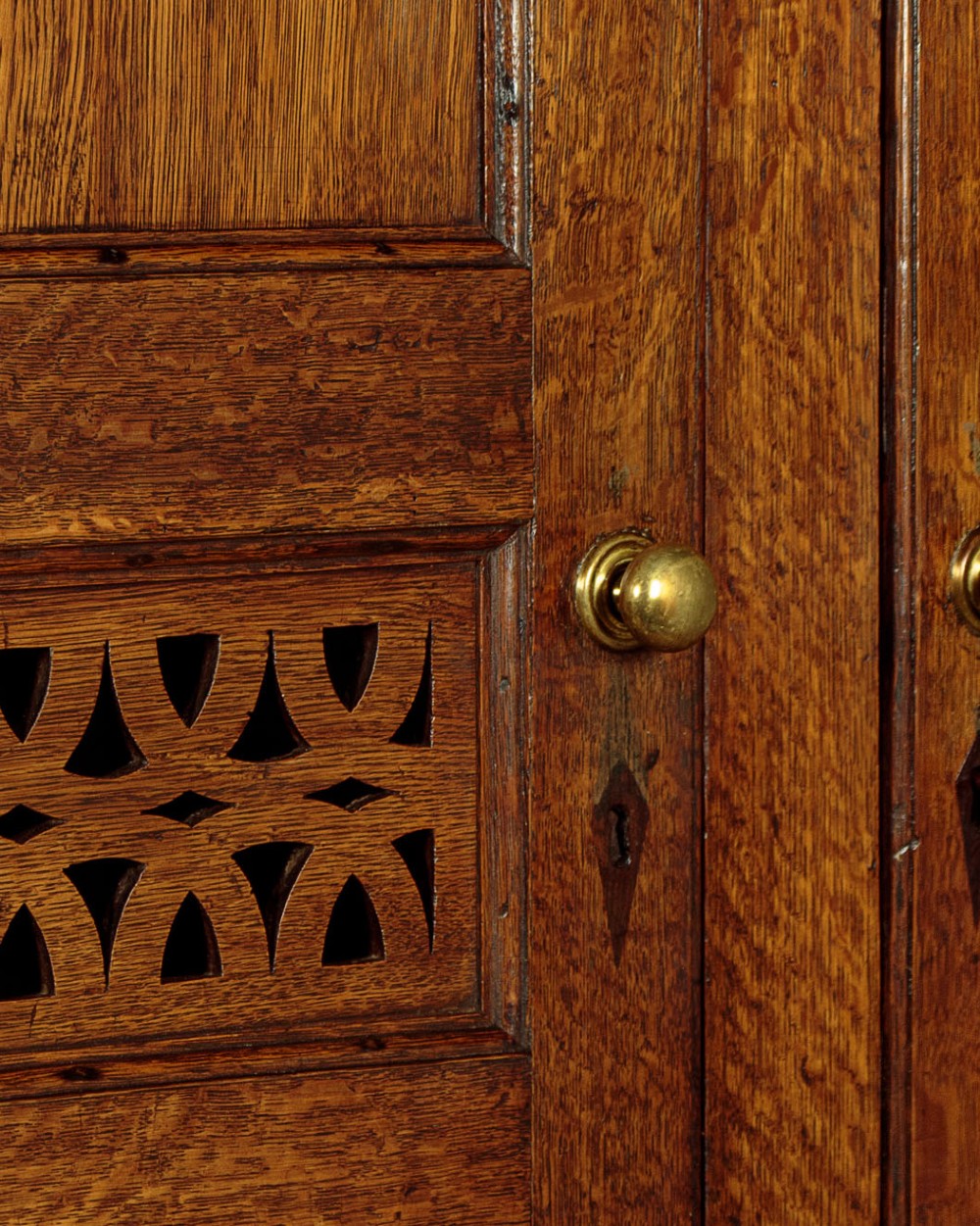 A two-part antique warm brown oak bread and cheese cupboard featuring upper doors with lattice ventilation fretwork over lower drawers and panelled cupboard doors. View VII