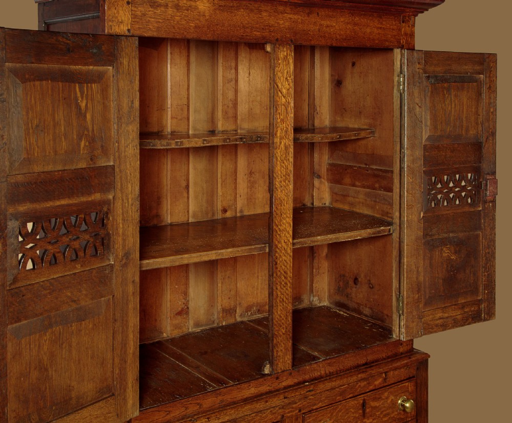 A two-part antique warm brown oak bread and cheese cupboard featuring upper doors with lattice ventilation fretwork over lower drawers and panelled cupboard doors. View VIII