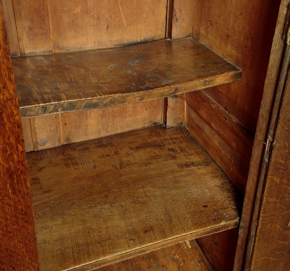 A two-part antique warm brown oak bread and cheese cupboard featuring upper doors with lattice ventilation fretwork over lower drawers and panelled cupboard doors. View IX