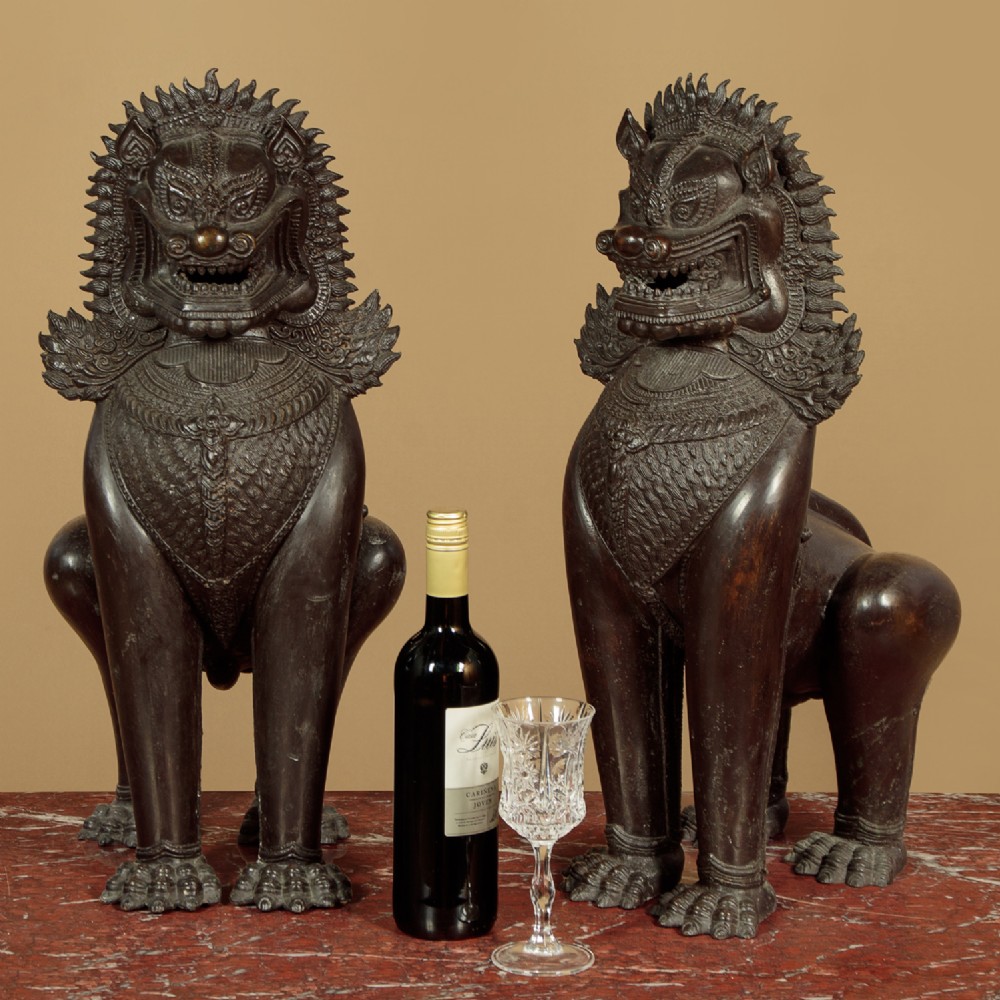 A pair of dark bronze temple lion statues sitting upright with intricate stylized manes and detailed ornamental chest bands. View II