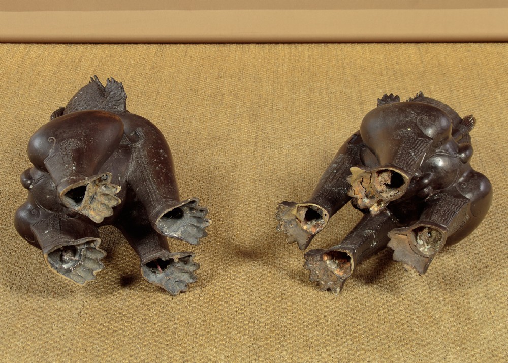 A pair of dark bronze temple lion statues sitting upright with intricate stylized manes and detailed ornamental chest bands. View XIII
