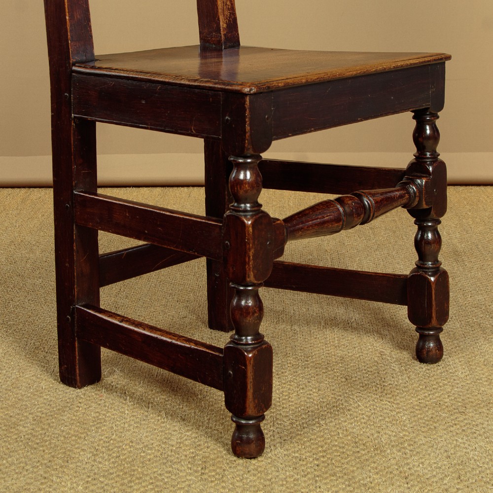 A set of four dark oak dining chairs featuring carved crest rails, arcaded spindle backs, wooden seats, and turned front legs. View IX
