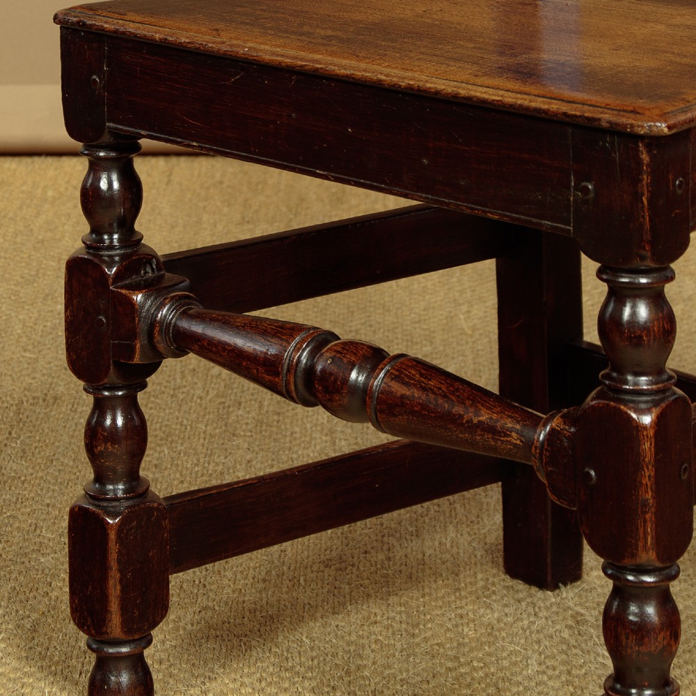 A set of four dark oak dining chairs featuring carved crest rails, arcaded spindle backs, wooden seats, and turned front legs. View X