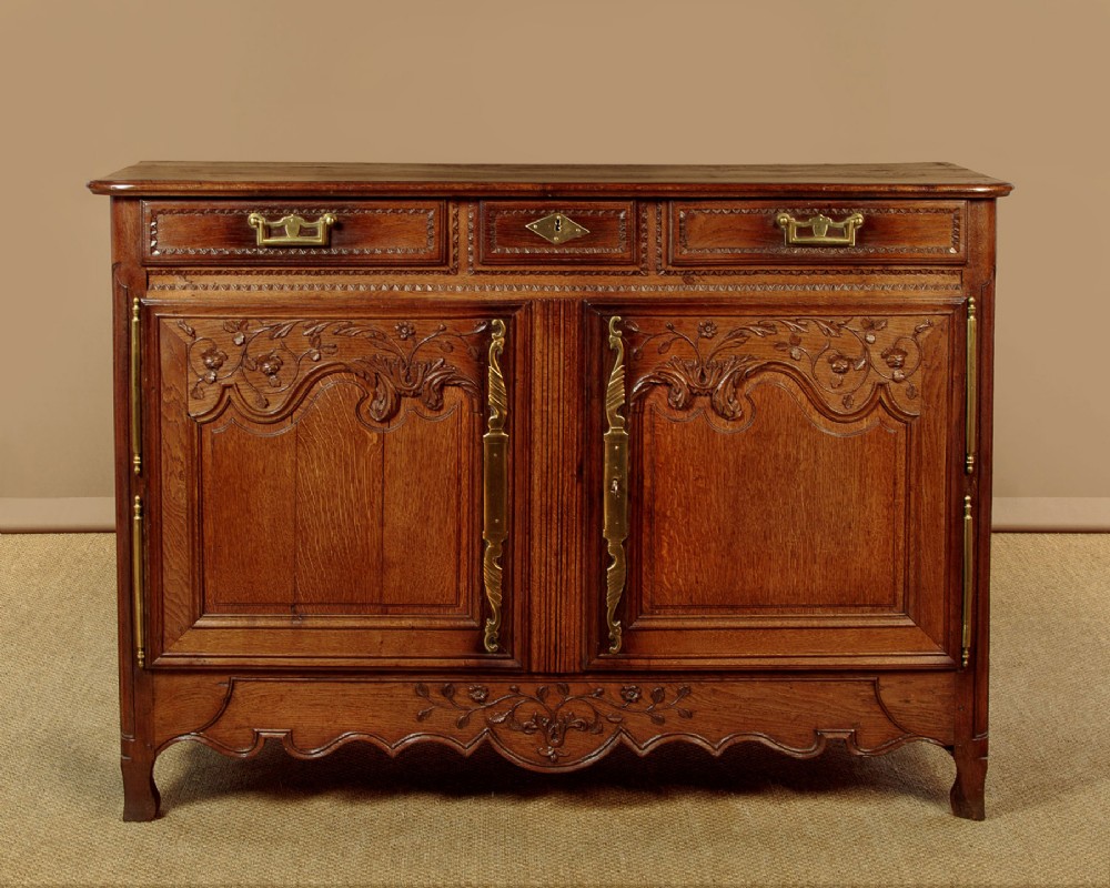 A late 18th-century French oak dresser base featuring two drawers above carved panelled cupboard doors with brass hardware.