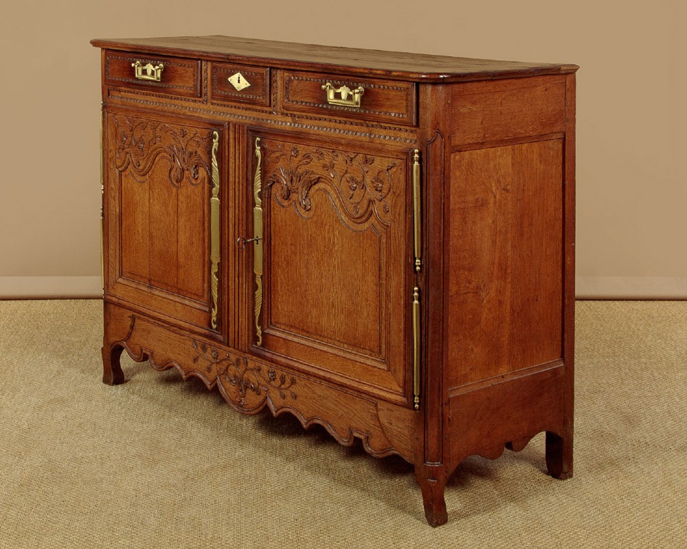 A late 18th-century French oak dresser base featuring two drawers above carved panelled cupboard doors with brass hardware. View II