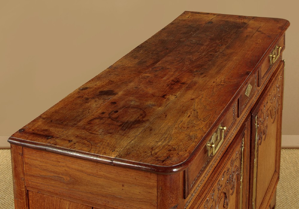 A late 18th-century French oak dresser base featuring two drawers above carved panelled cupboard doors with brass hardware. View V