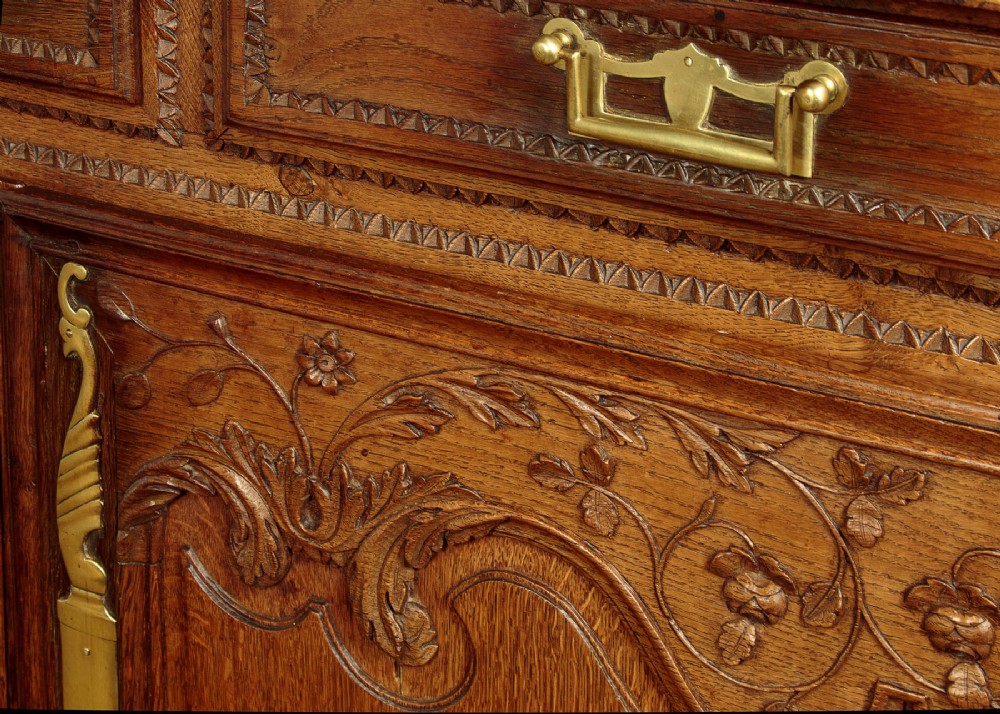 A late 18th-century French oak dresser base featuring two drawers above carved panelled cupboard doors with brass hardware. View X