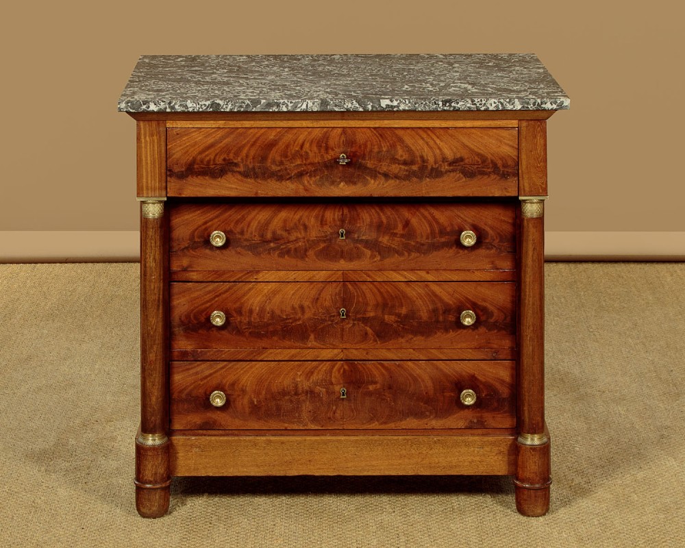 An Empire style mahogany chest of four drawers featuring a grey marble top, brass pull handles, and side column pillars.