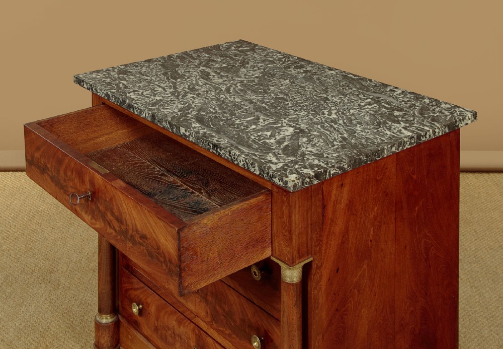 An Empire style mahogany chest of four drawers featuring a grey marble top, brass pull handles, and side column pillars. View V