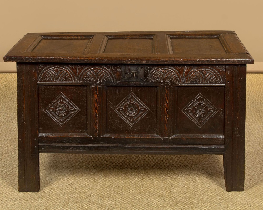 A dark carved oak 17th-century coffer featuring three lozenge-carved front panels, a lunette carved top rail, and a panelled hinged lid.
