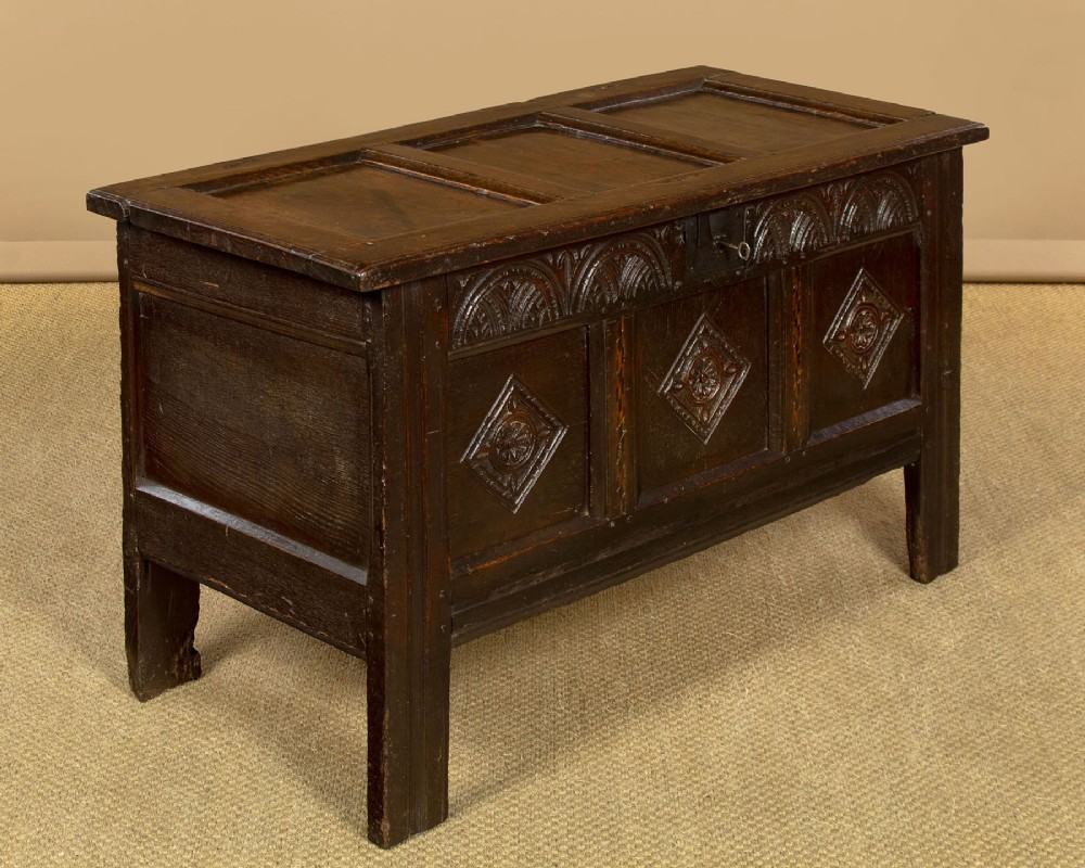 A dark carved oak 17th-century coffer featuring three lozenge-carved front panels, a lunette carved top rail, and a panelled hinged lid. View II