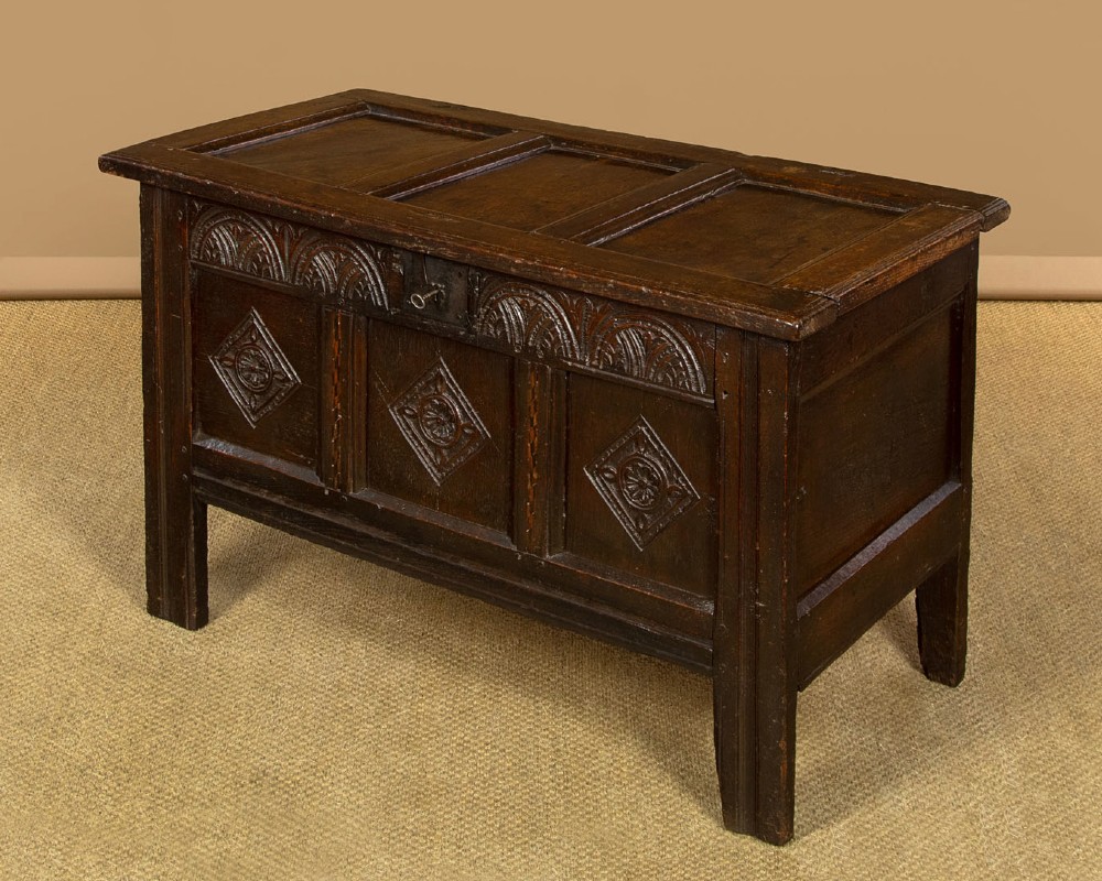 A dark carved oak 17th-century coffer featuring three lozenge-carved front panels, a lunette carved top rail, and a panelled hinged lid. View III