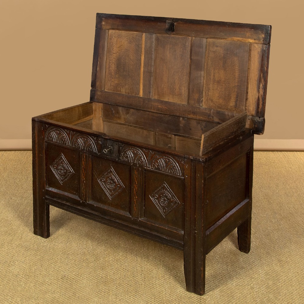 A dark carved oak 17th-century coffer featuring three lozenge-carved front panels, a lunette carved top rail, and a panelled hinged lid. View IV