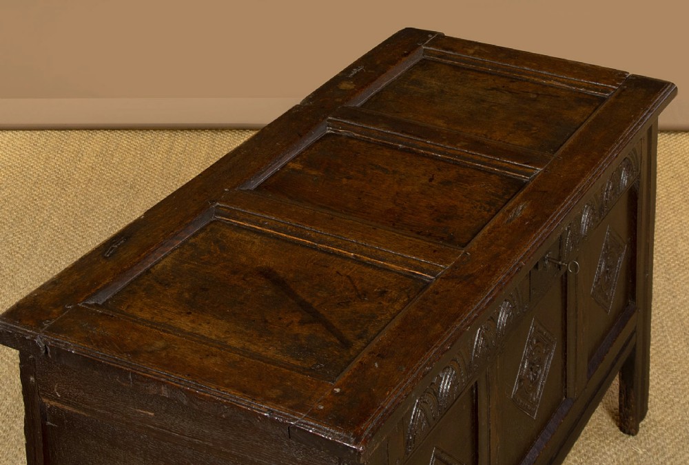 A dark carved oak 17th-century coffer featuring three lozenge-carved front panels, a lunette carved top rail, and a panelled hinged lid. View V