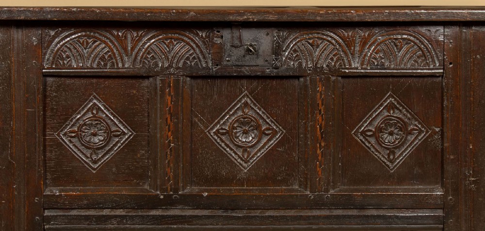 A dark carved oak 17th-century coffer featuring three lozenge-carved front panels, a lunette carved top rail, and a panelled hinged lid. View VII