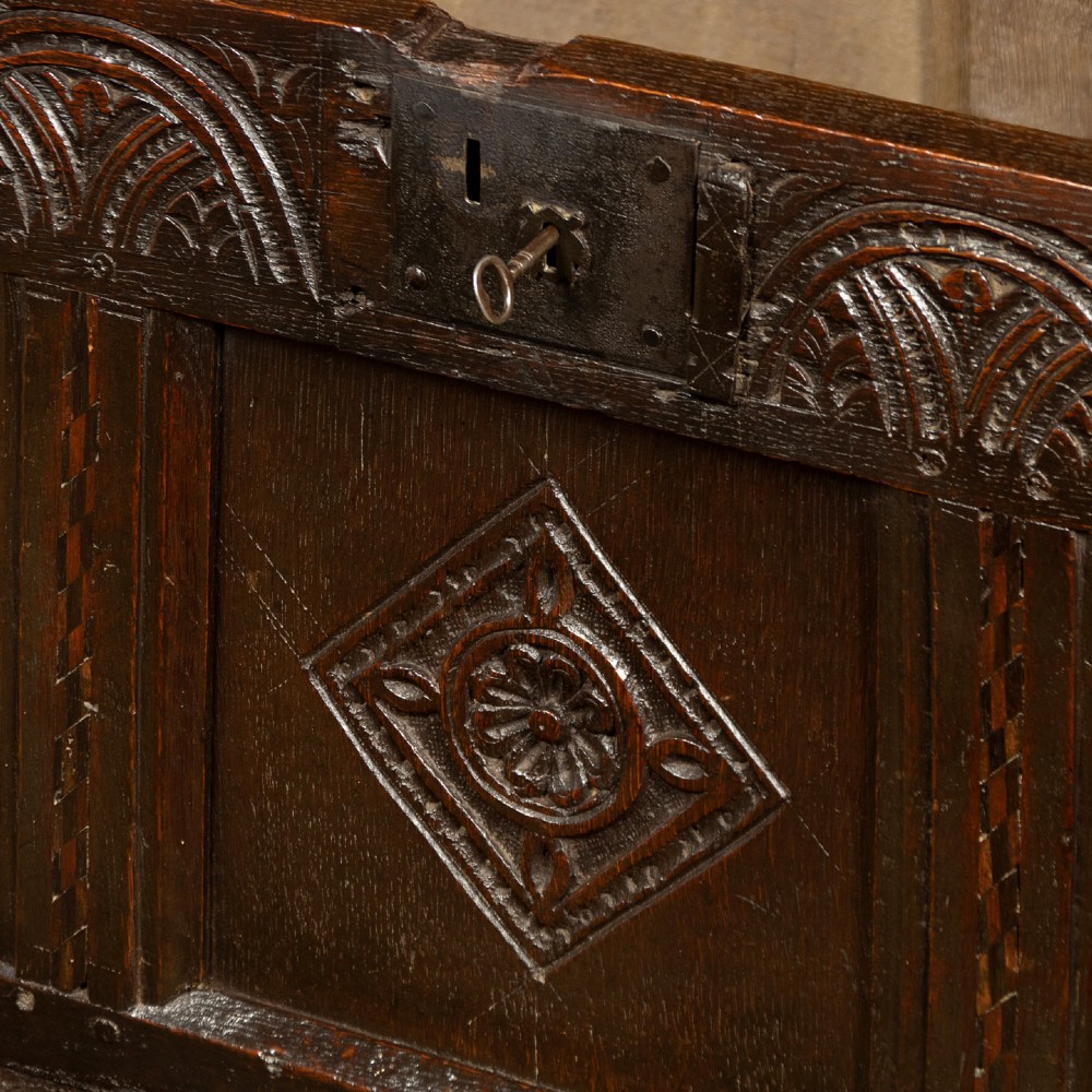 A dark carved oak 17th-century coffer featuring three lozenge-carved front panels, a lunette carved top rail, and a panelled hinged lid. View VIII