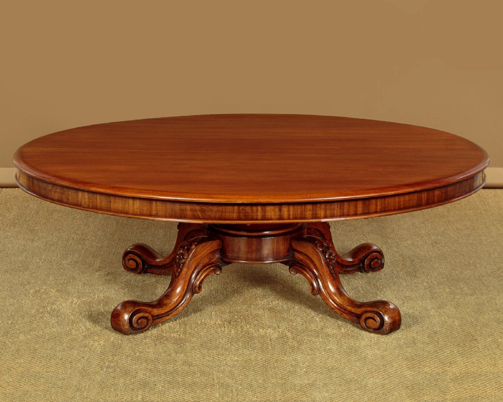 A large Victorian mahogany oval coffee table featuring a polished top, a deep apron, and a carved quadruped pedestal base with scroll feet.