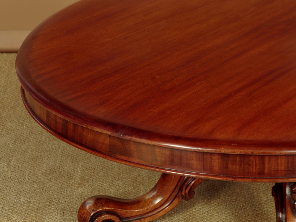 A large Victorian mahogany oval coffee table featuring a polished top, a deep apron, and a carved quadruped pedestal base with scroll feet. View V