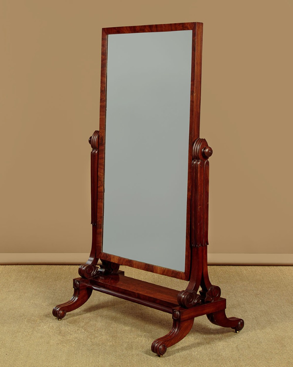 A 19th-century mahogany cheval mirror featuring a rectangular swivelling glass frame set between carved reeded uprights on scroll feet.