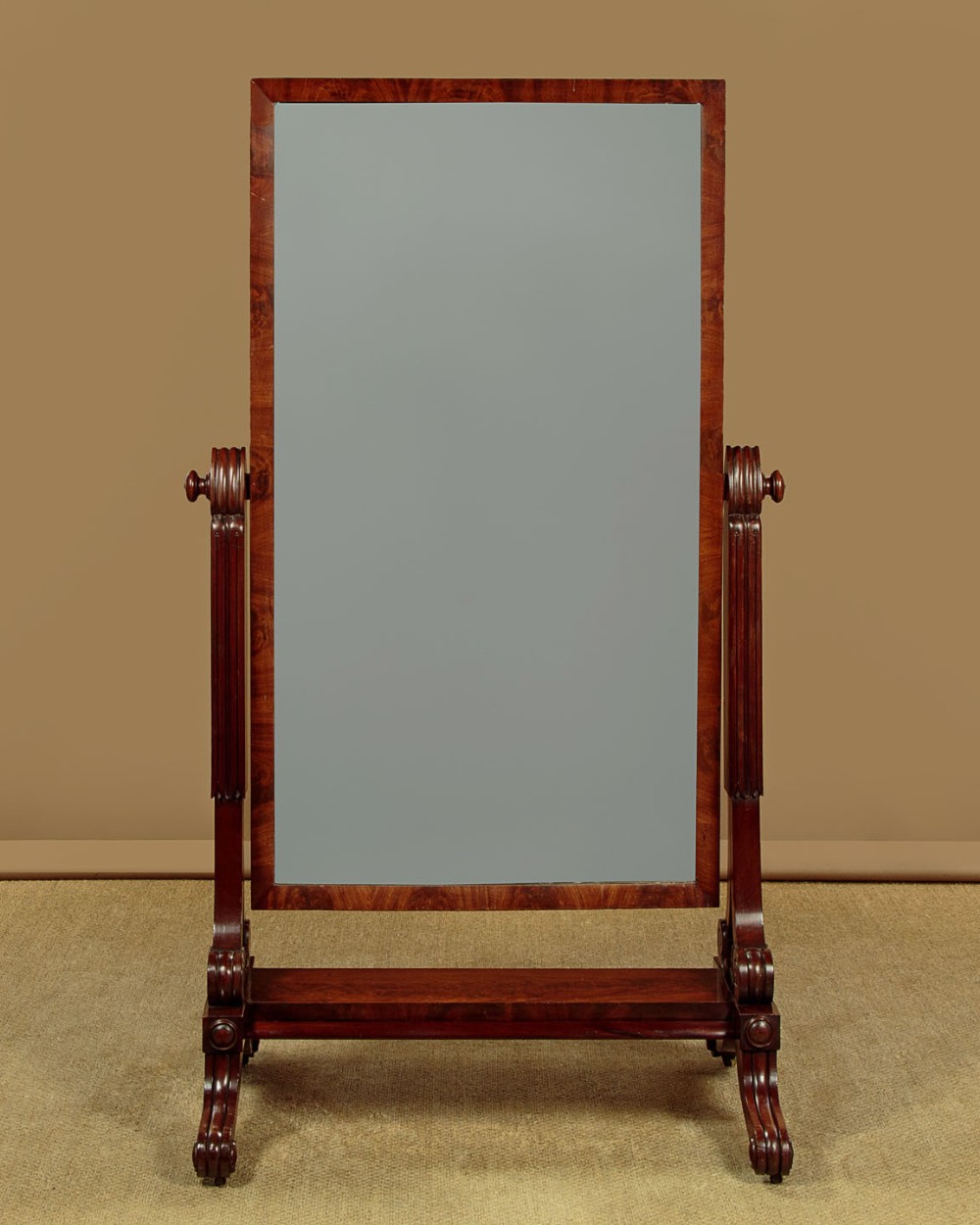 A 19th-century mahogany cheval mirror featuring a rectangular swivelling glass frame set between carved reeded uprights on scroll feet. View III