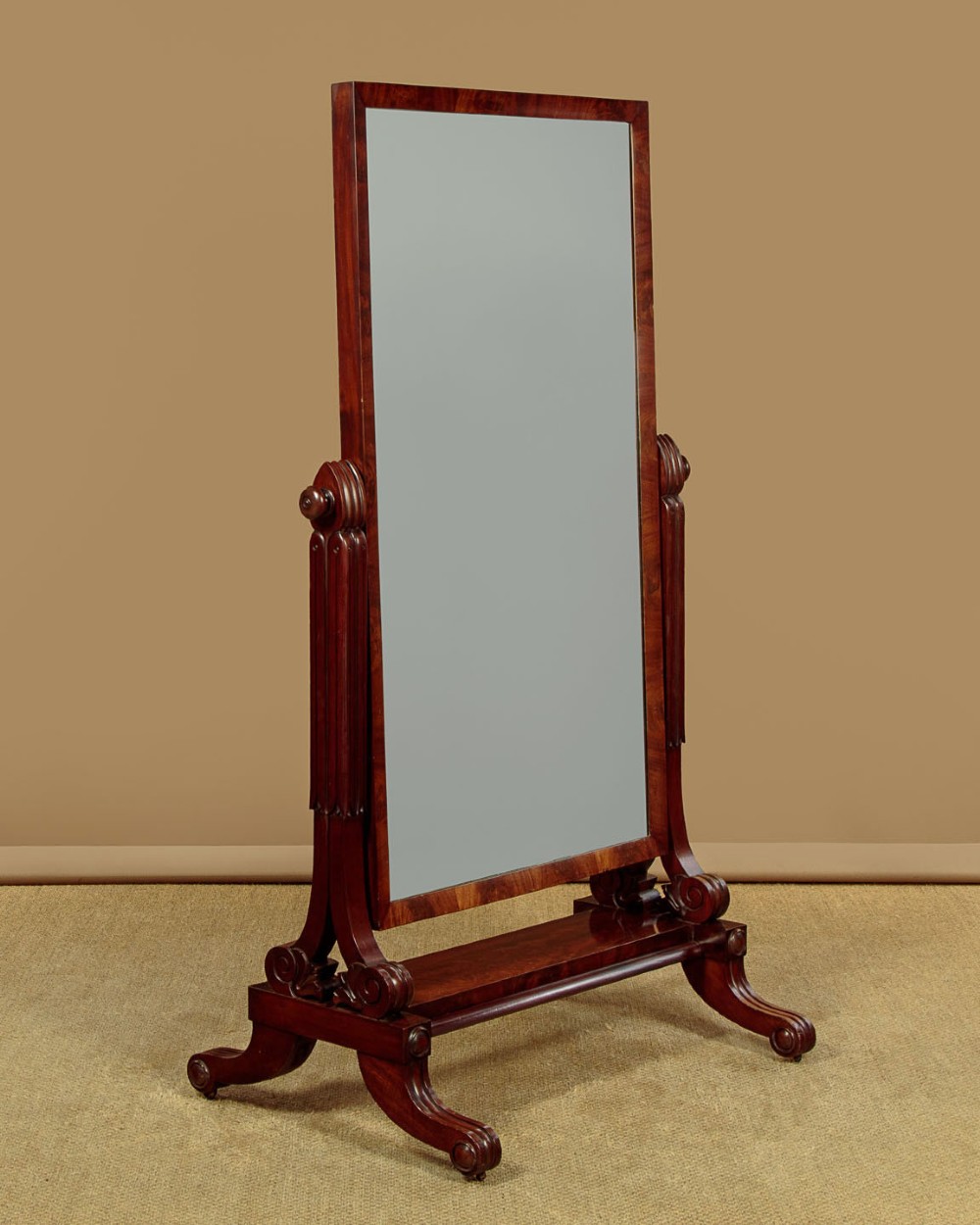 A 19th-century mahogany cheval mirror featuring a rectangular swivelling glass frame set between carved reeded uprights on scroll feet. View IV
