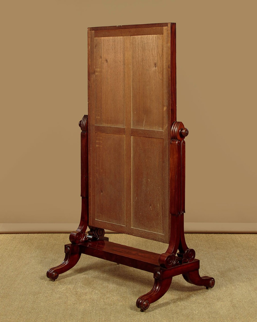 A 19th-century mahogany cheval mirror featuring a rectangular swivelling glass frame set between carved reeded uprights on scroll feet. View X
