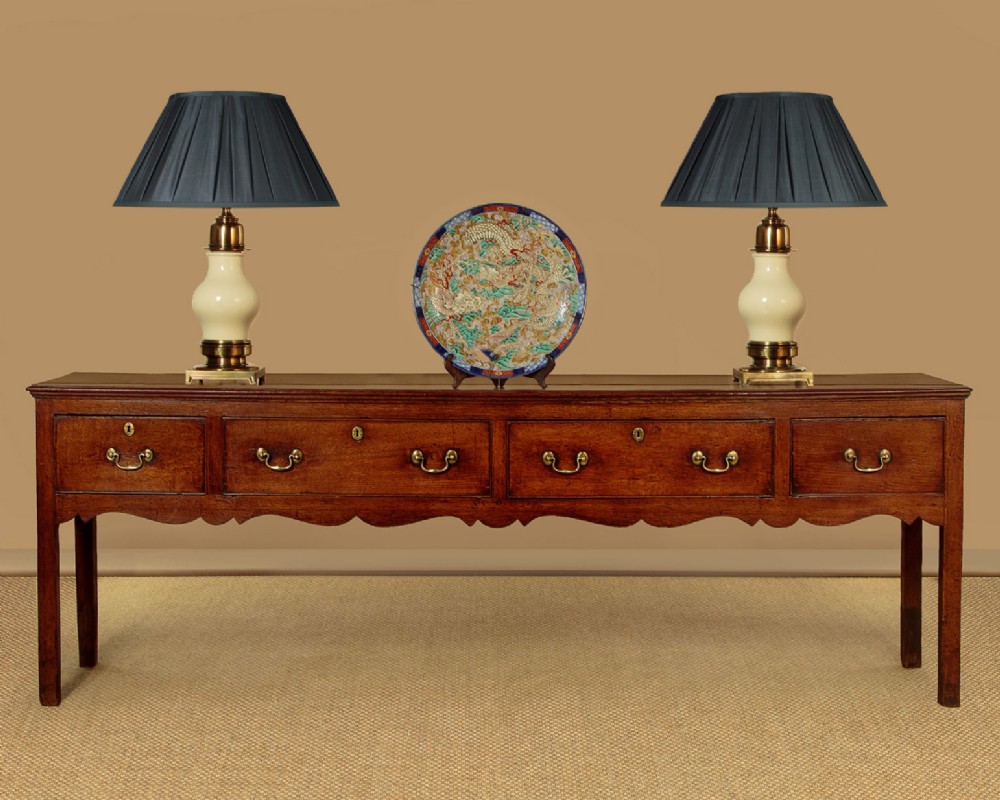 An 18th-century long oak dresser base featuring four drawers with brass swan-neck handles, a scalloped lower apron, and straight square legs. View II