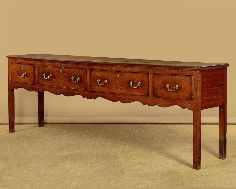 An 18th-century long oak dresser base featuring four drawers with brass swan-neck handles, a scalloped lower apron, and straight square legs. View III