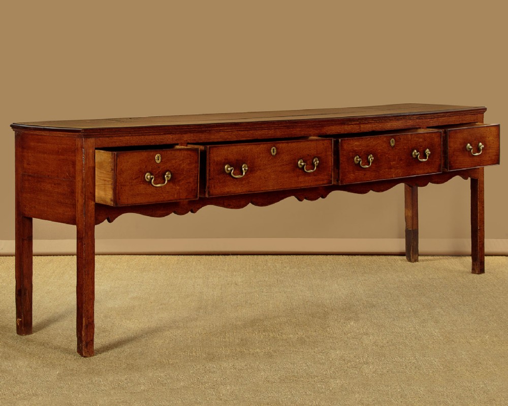 An 18th-century long oak dresser base featuring four drawers with brass swan-neck handles, a scalloped lower apron, and straight square legs. View IV
