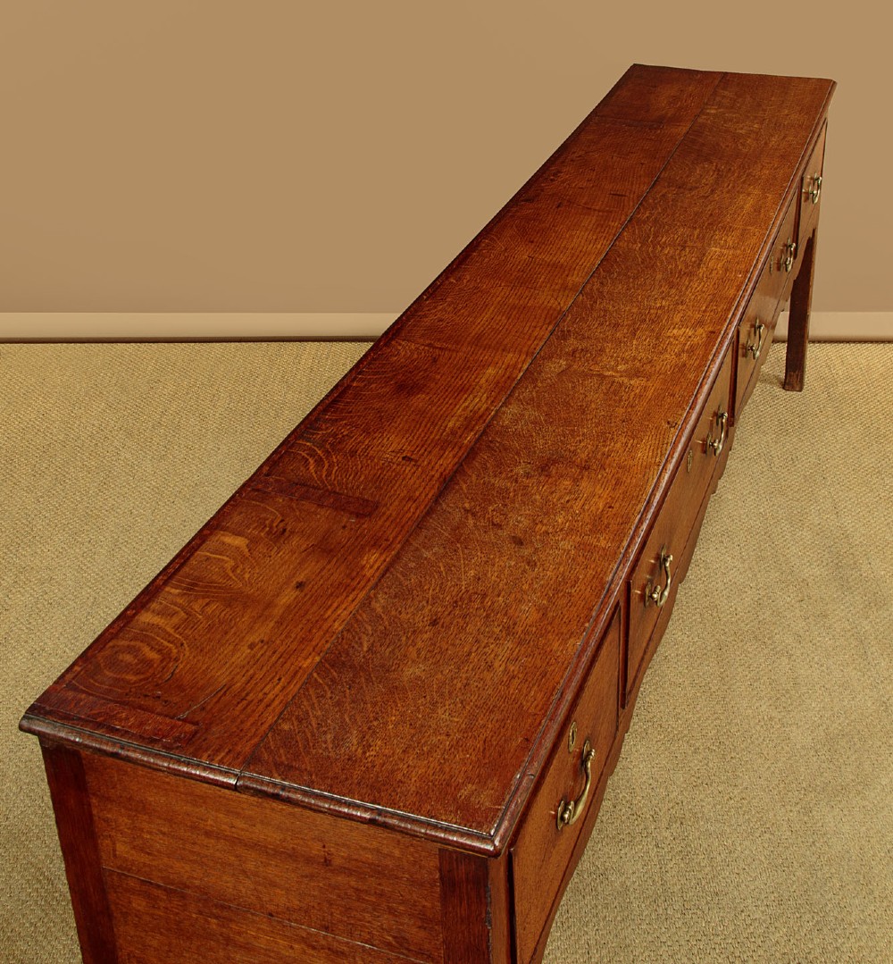 An 18th-century long oak dresser base featuring four drawers with brass swan-neck handles, a scalloped lower apron, and straight square legs. View V