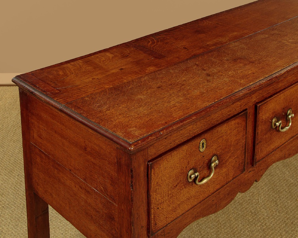 An 18th-century long oak dresser base featuring four drawers with brass swan-neck handles, a scalloped lower apron, and straight square legs. View VI