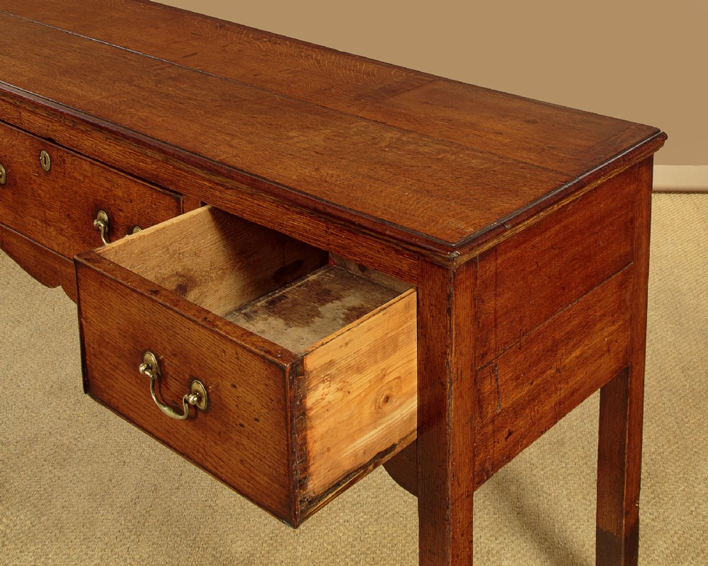 An 18th-century long oak dresser base featuring four drawers with brass swan-neck handles, a scalloped lower apron, and straight square legs. View VII