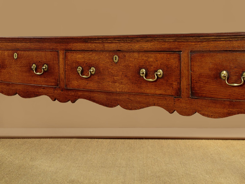 An 18th-century long oak dresser base featuring four drawers with brass swan-neck handles, a scalloped lower apron, and straight square legs. View VIII